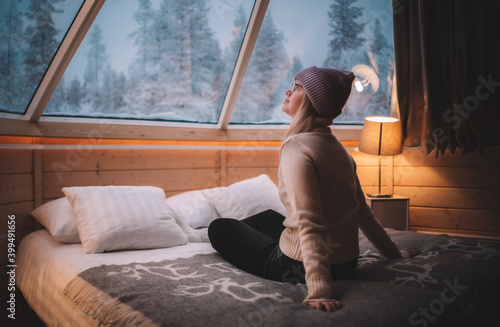 woman sitting and watching the landscape on the bed in the aurora cabin in Finland 