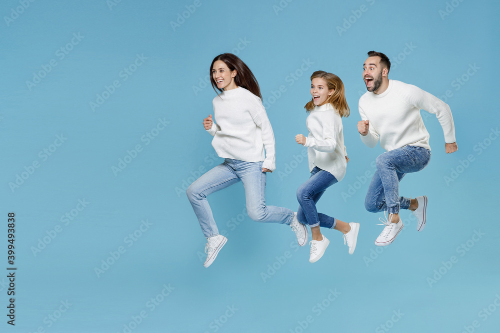 Full length of surprised young parents mom dad with child kid daughter teen girl in white sweaters jumping like running isolated on blue wall background studio portrait. Family day parenthood concept. Full length of surprised young parents mom dad with child kid daughter teen girl in white sweaters jumping like running isolated on blue wall background studio portrait. Family day parenthood concept.
