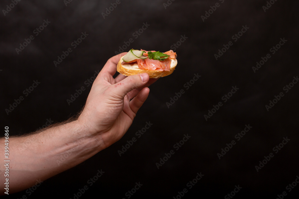 a man's hand on a black background holds a sandwich with a red fish a man's hand on a black background holds a sandwich with a red fish