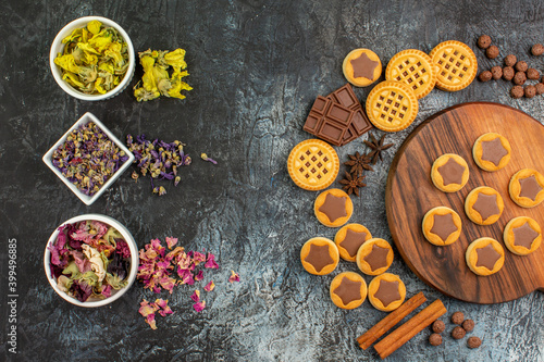 top view of dry flowers on bowls with cookies on wooden platter and sweets on grey background © Kamran