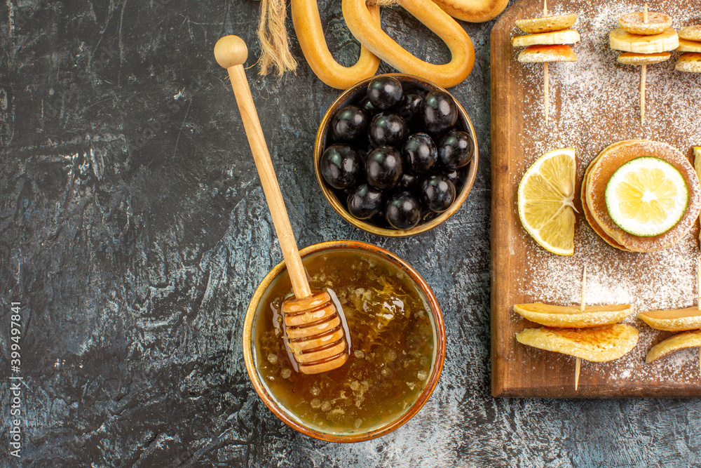 Half shot of fruit pancakes cookies near honey in a bowl and black cherries on gray table Half shot of fruit pancakes cookies near honey in a bowl and black cherries on gray table