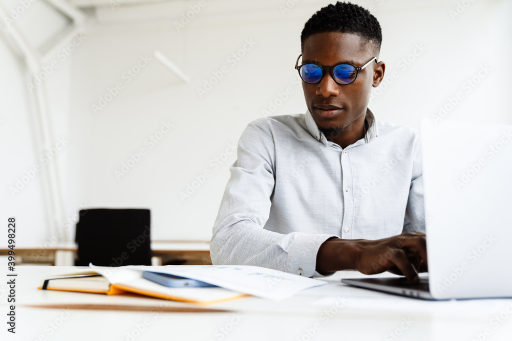 © Drobot Dean - Afro american focused man working with papers and laptop