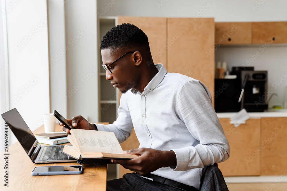 Afro american focused man using smartphone and reading book Afro american focused man using smartphone and reading book