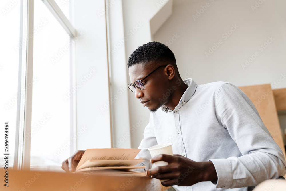 Afro american focused man reading book and drinking coffee Afro american focused man reading book and drinking coffee