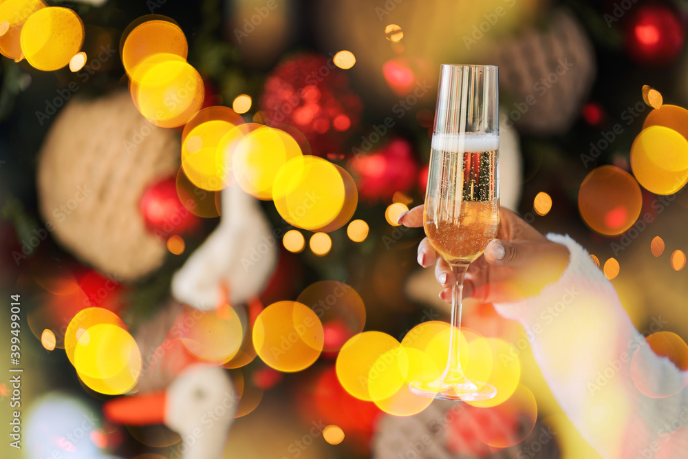 holding a glass in his hand against the background of a Christmas tree. Celebrates the holiday alone. Christmas lights are bright glow on the background