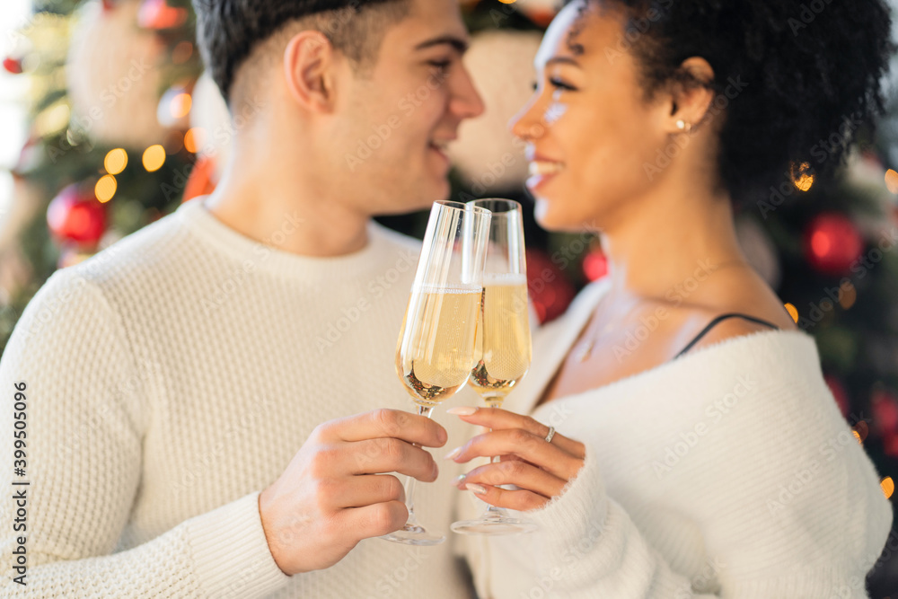 a young couple of friends hold glasses in their hands with a champagne drink and clink glasses. Christmas tree with toys is decorated for Christmas. celebrate the holiday of Christmas. a young couple of friends hold glasses in their hands with a champagne drink and clink glasses. Christmas tree with toys is decorated for Christmas. celebrate the holiday of Christmas.