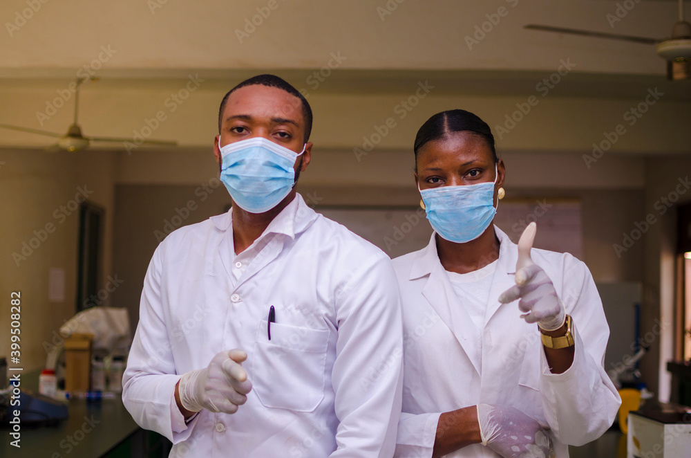 close up of two african doctors wearing face mask to prevent themselves while in the laboratory feeling happy while they did thumbs up
