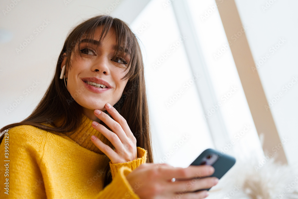 Charming happy girl in earphones using mobile phone and smiling Charming happy girl in earphones using mobile phone and smiling