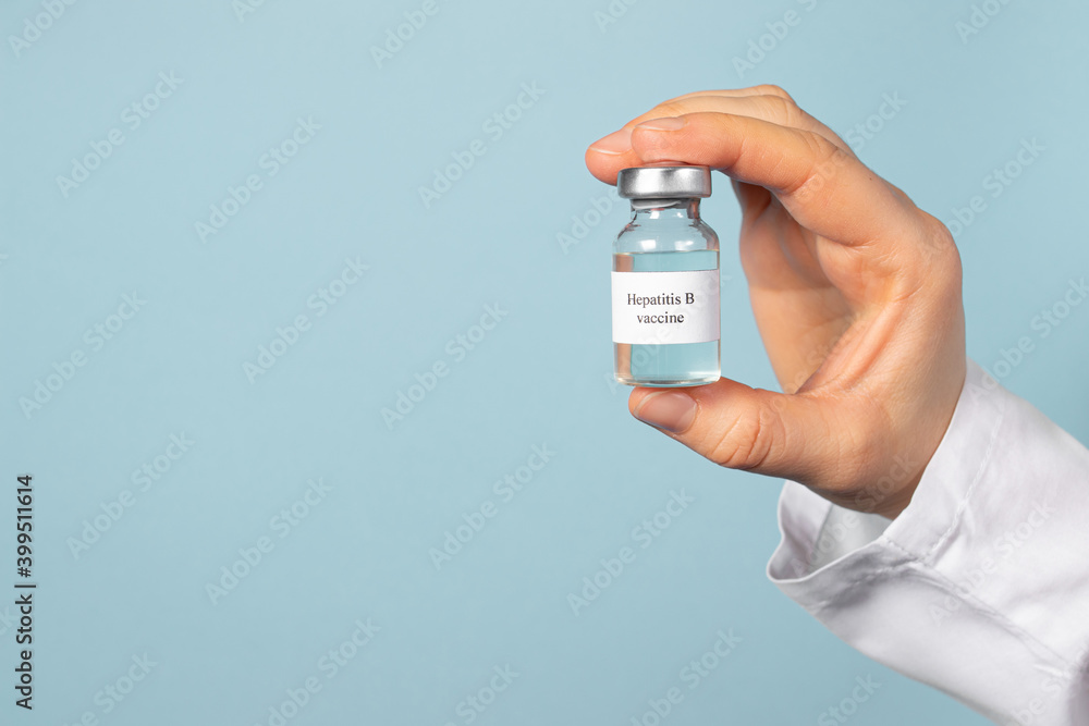 A doctor or laboratory technician holds a vial with a hepatitis B vaccine in his hand. With a place for text on a blue background. A doctor or laboratory technician holds a vial with a hepatitis B vaccine in his hand. With a place for text on a blue background.