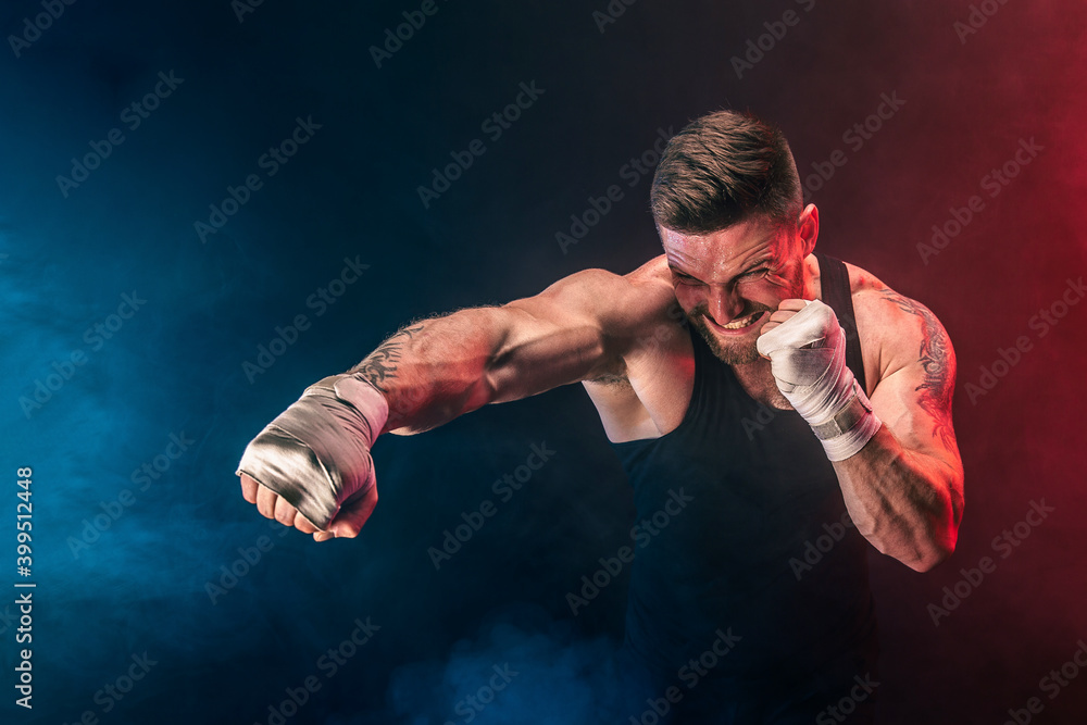 Bearded tattooed portsman muay thai boxer in black undershirt and boxing gloves fighting on dark background with smoke. Sport concept.