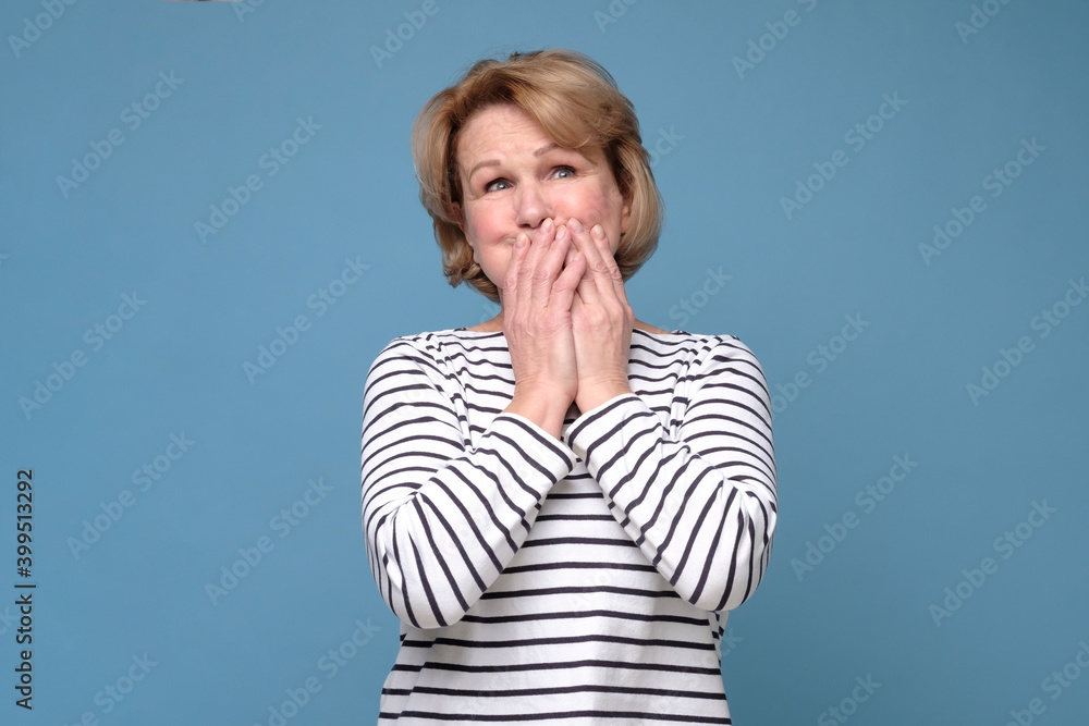 Senior woman giggle covering mouth with hands. Gossip concept. Studio shot on blue wall. Senior woman giggle covering mouth with hands. Gossip concept. Studio shot on blue wall.