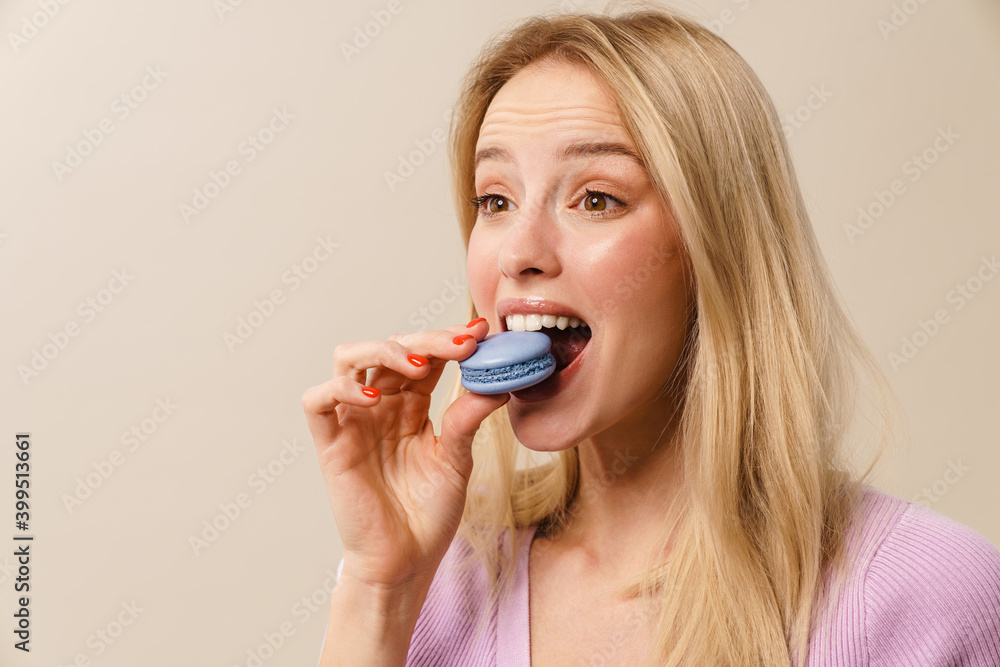 Cheerful beautiful girl grimacing while eating macaroon