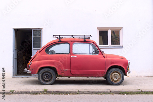 Old, vintage, red car in front of white wall white dor and small window.