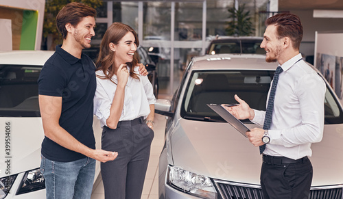 Young couple speaking with manager in car dealership