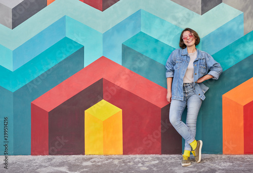 Cheerful young woman leaning on colorful wall