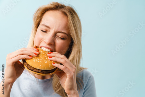 Beautiful hungry blonde girl eating hamburger on camera