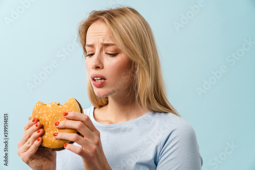 Unhappy beautiful blonde girl eating hamburger on camera