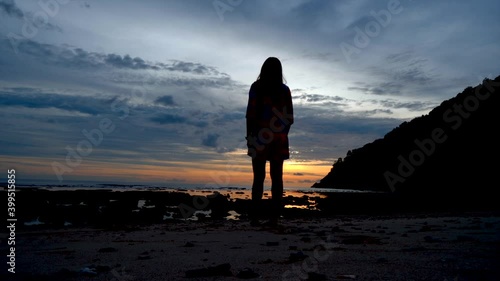 Silhouettte girl walking on the beach with a sand and rock in the evening sunset