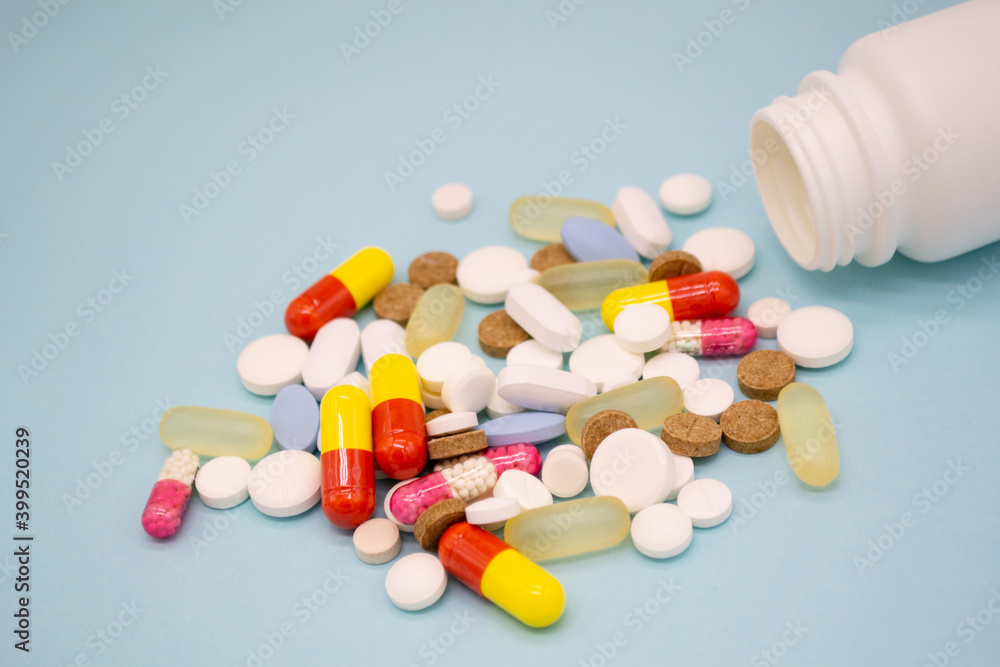 Multicolored pills fall out of a white bottle on a blue background Multicolored pills fall out of a white bottle on a blue background