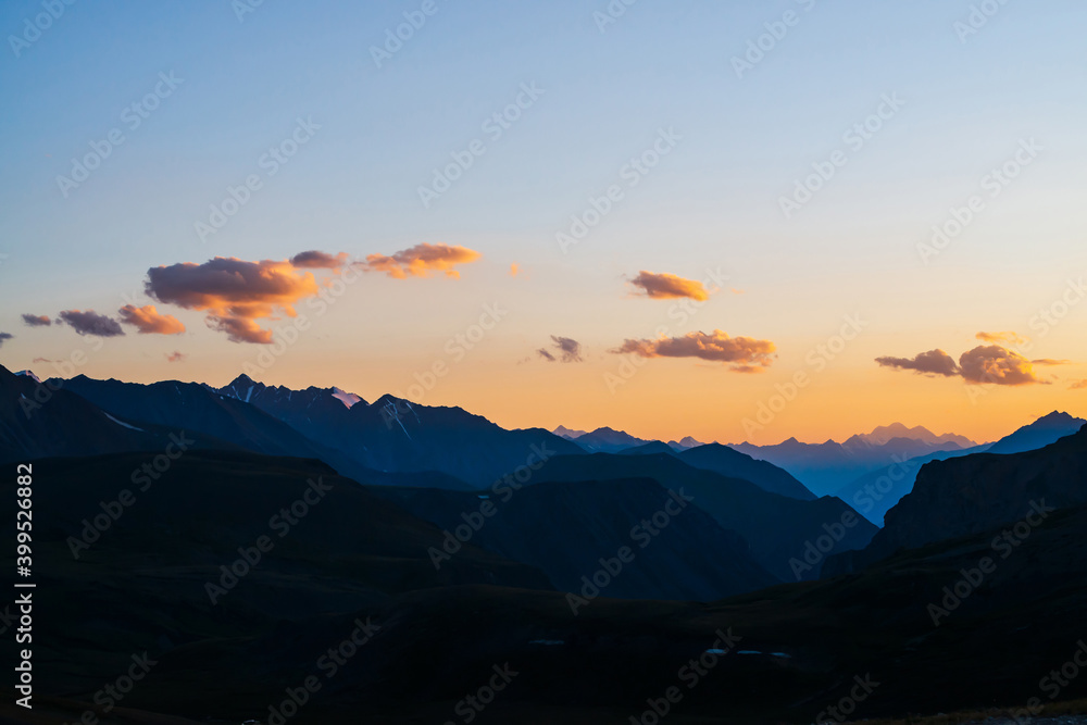 Colorful dawn landscape with beautiful mountains silhouettes and golden blue gradient sky with clouds. Vivid mountain scenery with picturesque multicolor sunset. Scenic sunrise view to mountain range.