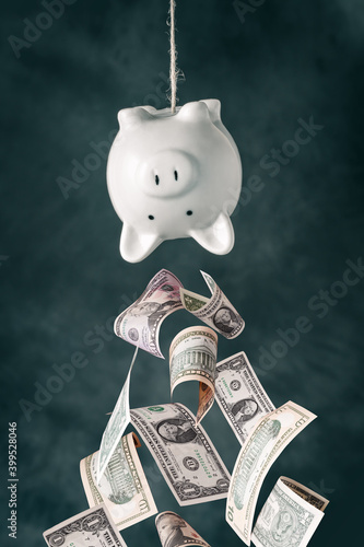 Dollar banknotes falling out of the upside down piggy bank
