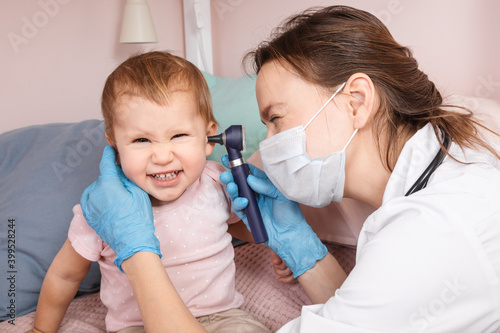 Pediatrician checking ear of baby girl with otoscope performing ENT exam at home during lockdown