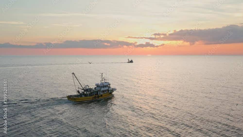 Fishing Boat with Large Catch Fish Swirling Flock Gulls Aerial View Drone Sunset Winter. Small Ship Floats on Sea Surface Golden Sky Leaving a Path of Sea Foam Water. Seagulls. Bright Disk of Sun Fishing Boat with Large Catch Fish Swirling Flock Gulls Aerial View Drone Sunset Winter. Small Ship Floats on Sea Surface Golden Sky Leaving a Path of Sea Foam Water. Seagulls. Bright Disk of Sun