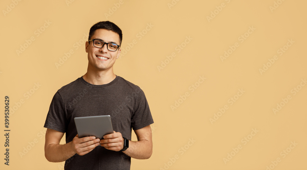 Cheerful young attractive man in glasses looks at camera, holds digital tablet on online lesson - obrazy, fototapety, plakaty 