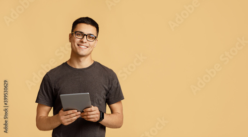 Cheerful young attractive man in glasses looks at camera, holds digital tablet on online lesson