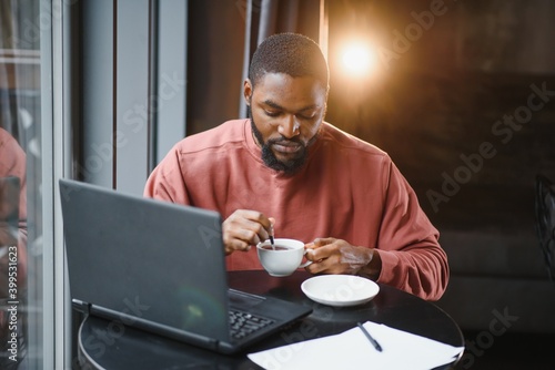 Portrait of happy african businessman using phone while working on laptop in restaurant