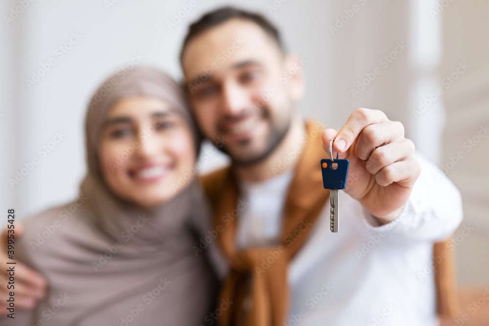 Joyful Muslim Couple Showing New House Key Standing Indoors Joyful Muslim Couple Showing New House Key Standing Indoors