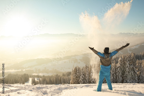 Happy Man standing in deep snow throwing snow into sunrise sunlight. Beautiful Winter Mountain Landscape. Allgau, Bavaria, Alps, Germany.