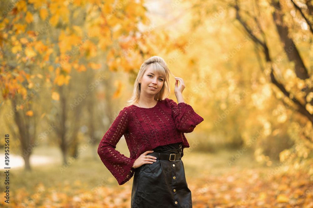 Blonde girl in a maroon sweater in the Park in autumn among the yellow leaves Blonde girl in a maroon sweater in the Park in autumn among the yellow leaves