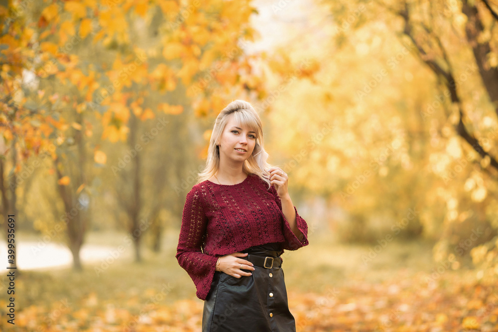 Blonde girl in a maroon sweater in the Park in autumn among the yellow leaves Blonde girl in a maroon sweater in the Park in autumn among the yellow leaves