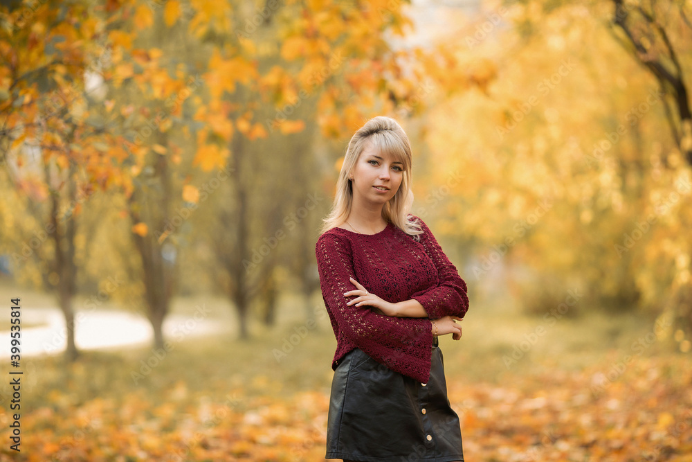 Blonde girl in a maroon sweater in the Park in autumn among the yellow leaves Blonde girl in a maroon sweater in the Park in autumn among the yellow leaves