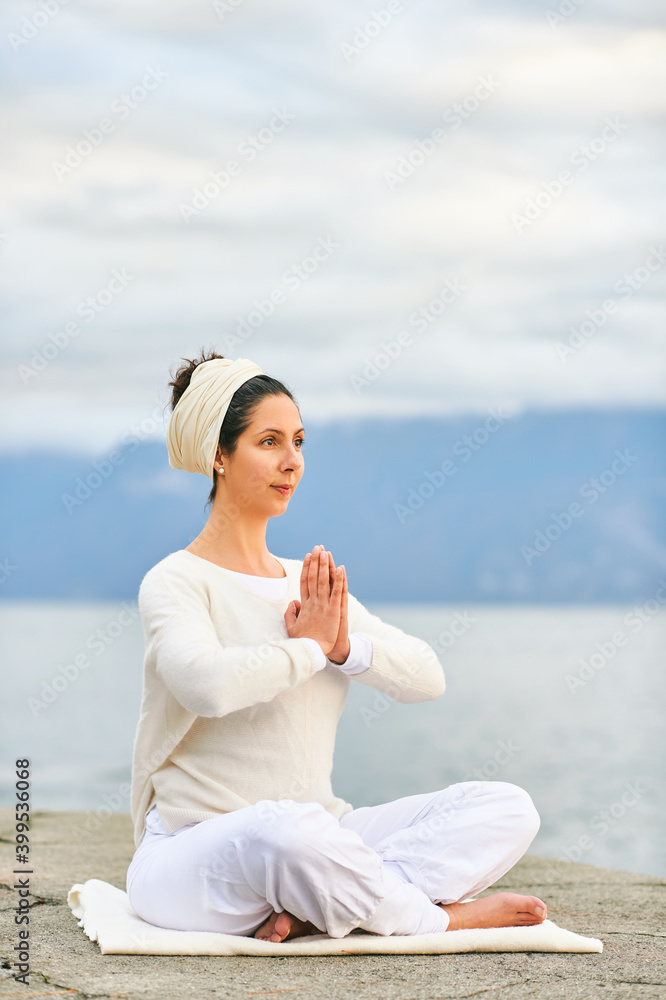 Concentrated woman meditating by the sea or lake, wearing white clothes