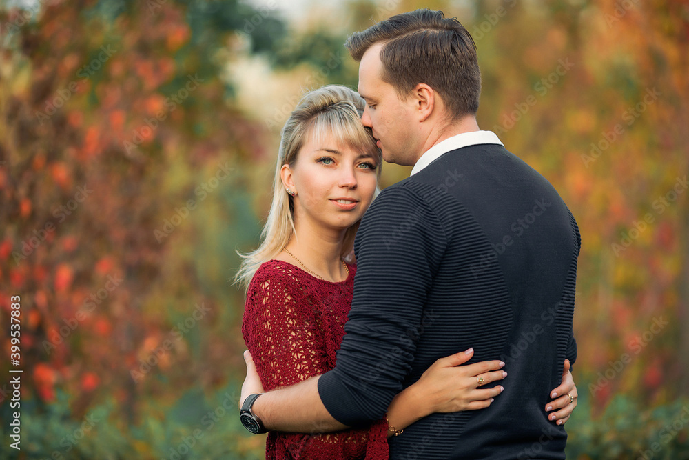 blonde girl in maroon sweater, brown-haired young man in blue sweater hug in the Park blonde girl in maroon sweater, brown-haired young man in blue sweater hug in the Park