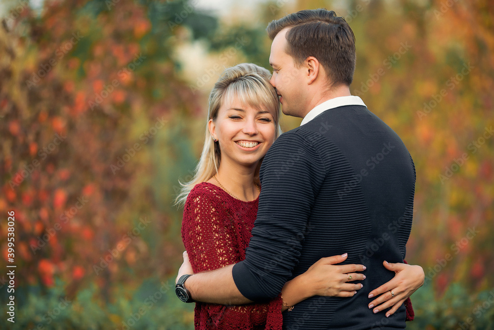 blonde girl in maroon sweater, brown-haired young man in blue sweater hug in the Park blonde girl in maroon sweater, brown-haired young man in blue sweater hug in the Park