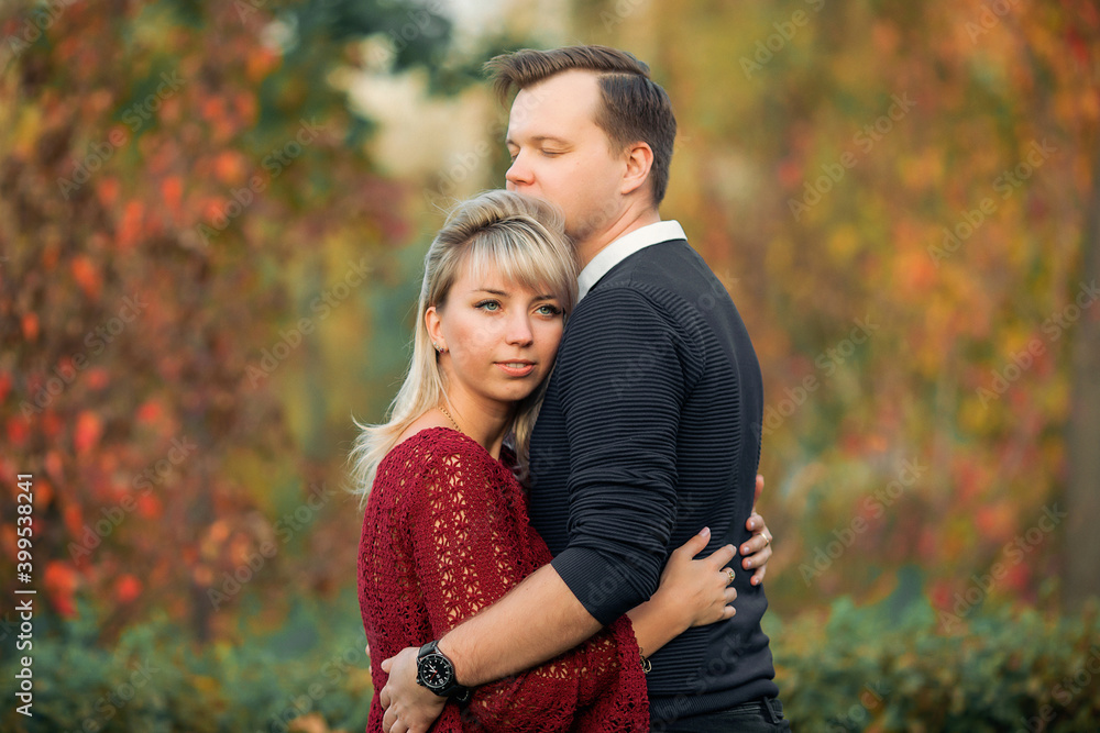 blonde girl in maroon sweater, brown-haired young man in blue sweater hug in the Park blonde girl in maroon sweater, brown-haired young man in blue sweater hug in the Park
