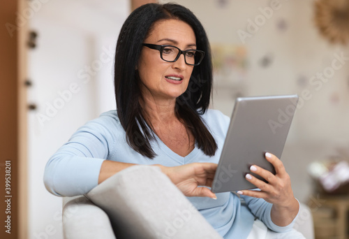 Mature woman sitting on couch and working on tablet