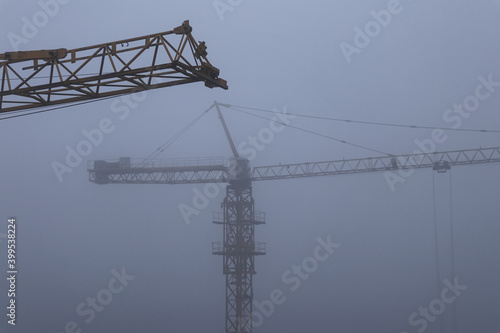 Construction cranes in the fog against the dark gray sky © Svitlana Ozirna