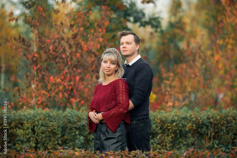 blonde girl in maroon sweater, brown-haired young man in blue sweater hug in the Park