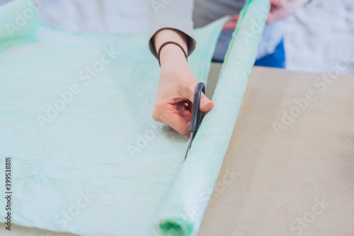 Professional woman floral artist, florist cutting packing paper for bouquet on table at workshop, flower shop - close up view. Floristry, handmade and small business concept