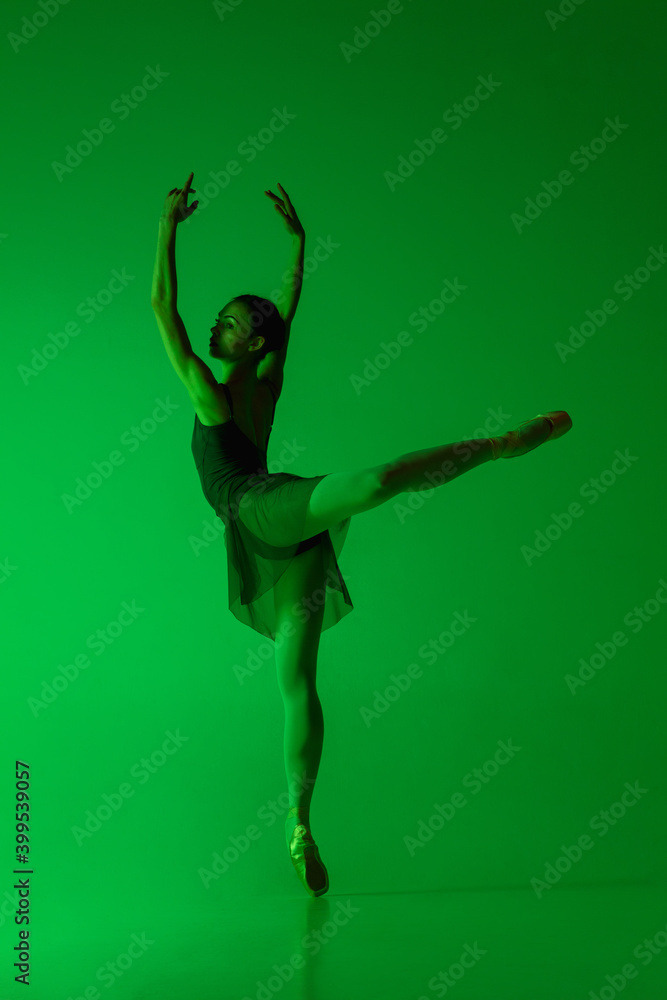 Gorgeous. Young and graceful ballet dancer isolated on gradient green studio background in neon. Art, motion, action, flexibility, inspiration concept. Flexible ballerina, weightless jumps. Gorgeous. Young and graceful ballet dancer isolated on gradient green studio background in neon. Art, motion, action, flexibility, inspiration concept. Flexible ballerina, weightless jumps.