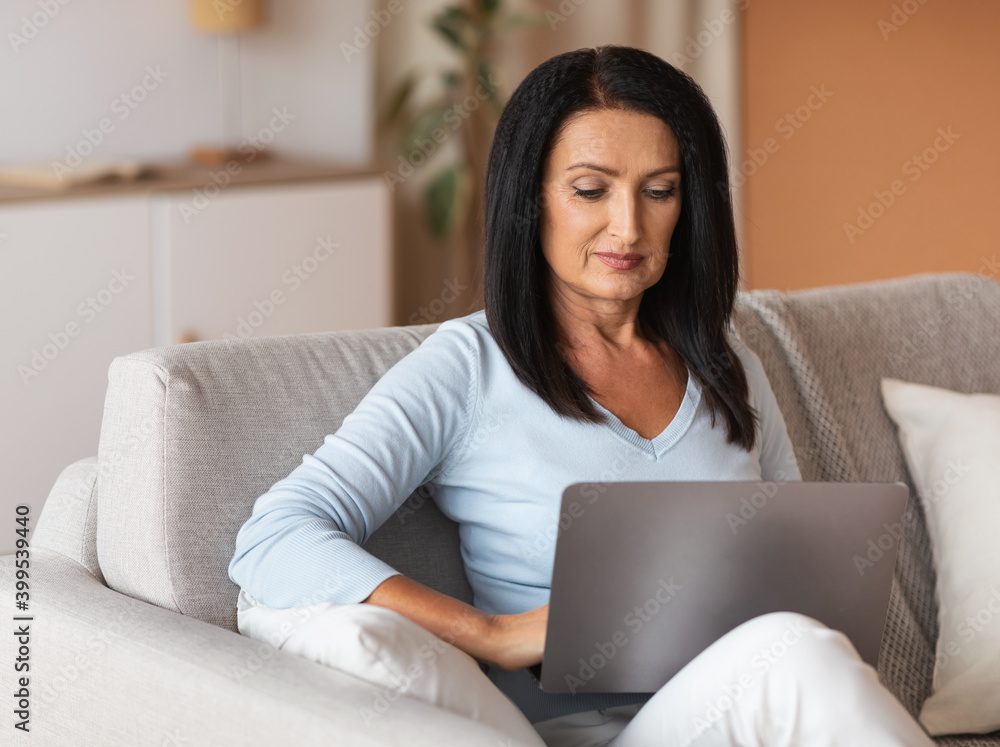 Mature woman sitting on couch and working on computer Mature woman sitting on couch and working on computer