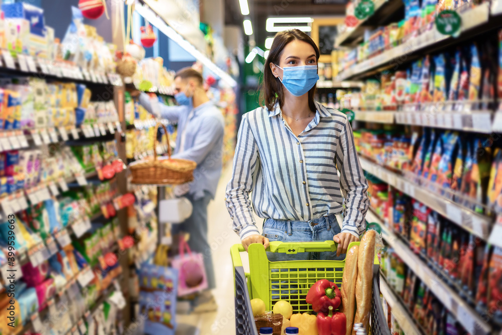 Young woman in mask with the cart shopping in supermarket