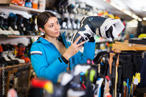 Young girl choosing ski boots for skiing in store of sports equipment.