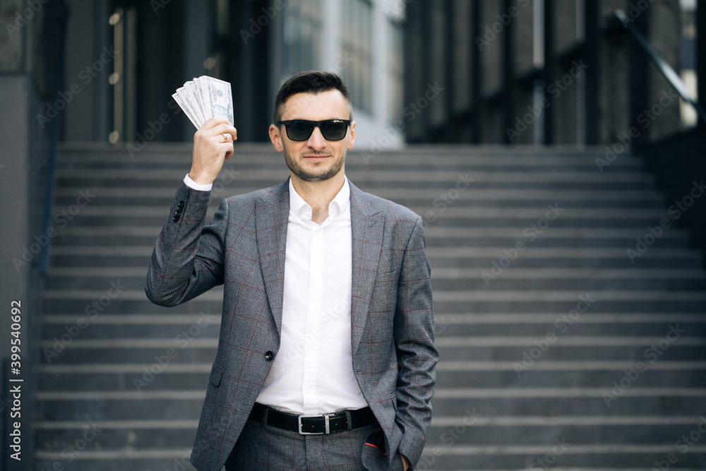 Lifestyle, richness, joy, success. Happy rich successful man holds dollars outdoors. Portrait of satisfied businessman holds money. Lifestyle, richness, joy, success. Happy rich successful man holds dollars outdoors. Portrait of satisfied businessman holds money.