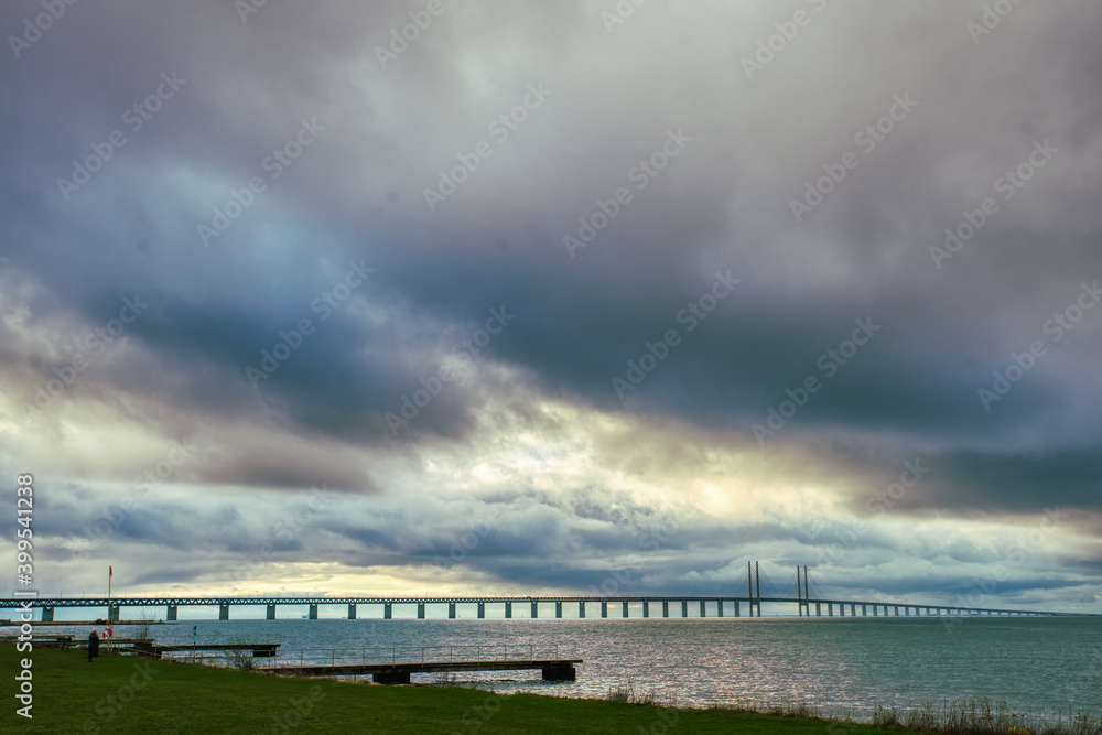 The Oresund Bridge in the Baltic Sea captured from Sibbarp, Limhamn against a cloudy dramatic sky. The Oresundsbron (Oresundsbroen) is a connection across the Oresund Strait between Sweden and Denmark The Oresund Bridge in the Baltic Sea captured from Sibbarp, Limhamn against a cloudy dramatic sky. The Oresundsbron (Oresundsbroen) is a connection across the Oresund Strait between Sweden and Denmark