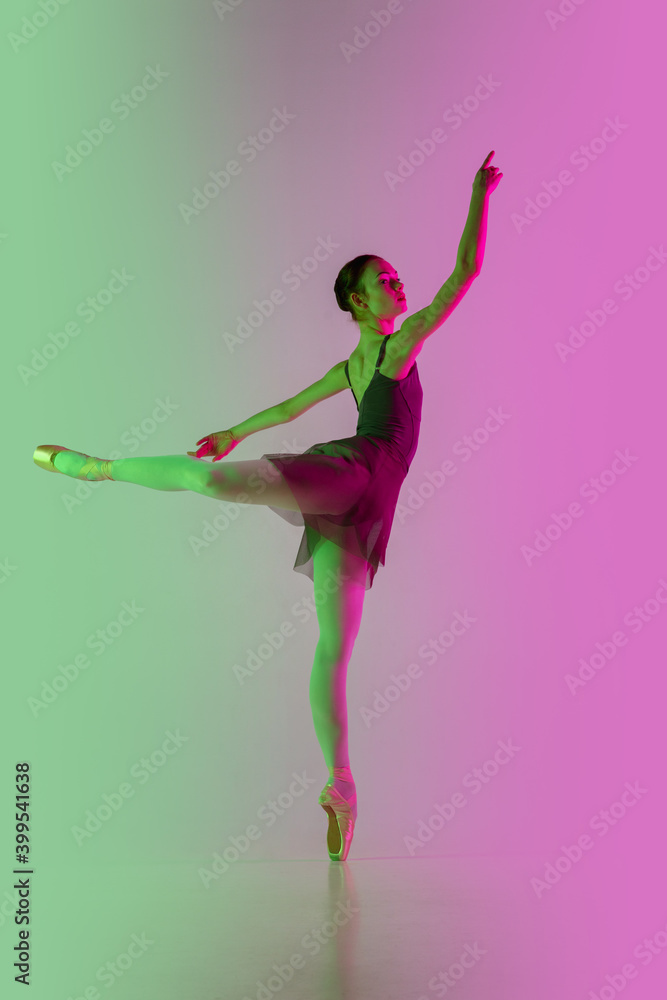 Feminine. Young and graceful ballet dancer isolated on gradient pink-green studio background in neon. Art, motion, action, flexibility, inspiration concept. Flexible ballerina, weightless jumps.